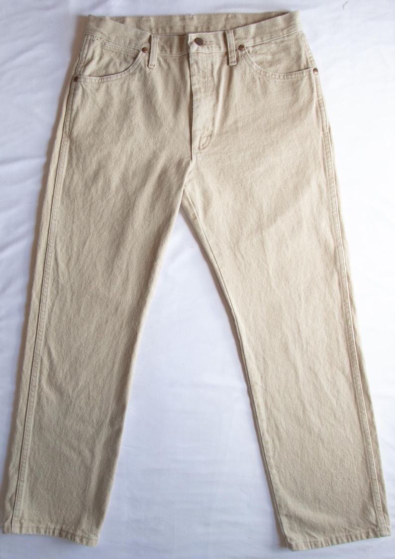 Op de afbeelding: Een beige spijkerbroek met een klassiek ontwerp met vijf zakken, een knoopsluiting en koperkleurige metalen klinknagels op de hoeken van de zakken. De broek heeft een recht model met zichtbare stiksels langs de zijnaden en de tailleband.