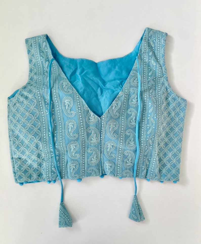Pu&ograve; includere: Un top senza maniche azzurro con ricami bianchi intricati. Il top presenta uno scollo a V e nappe decorative. Il tessuto presenta un motivo paisley e geometrico. &Egrave; un capo leggero e arioso.