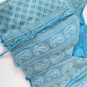 Pu&ograve; includere: Top ricamato azzurro con intricati motivi floreali e paisley bianchi. Il top presenta uno scollo a V ed &egrave; adornato da piccoli pompon blu lungo i bordi. Include una chiusura con lacci ed &egrave; realizzato in un tessuto morbido e leggero.