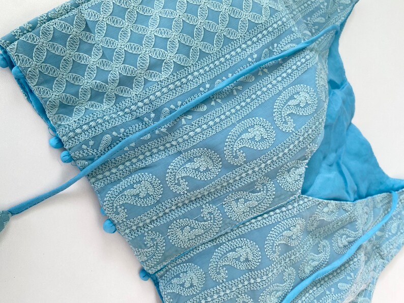 Pu&ograve; includere: Top ricamato azzurro con intricati motivi floreali e paisley bianchi. Il top presenta uno scollo a V ed &egrave; adornato da piccoli pompon blu lungo i bordi. Include una chiusura con lacci ed &egrave; realizzato in un tessuto morbido e leggero.