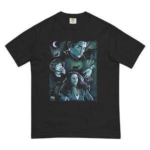 May include: Black t-shirt featuring a graphic illustration with characters from a fantasy movie. The design includes a forest scene with a crescent moon, wolves, and several people. The artwork is in shades of blue and green.