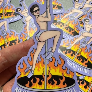 May include: A sticker featuring a person in sunglasses dancing on a pole, surrounded by flames. The sticker has a purple background and the text "SINCE I'M GOING TO HELL".