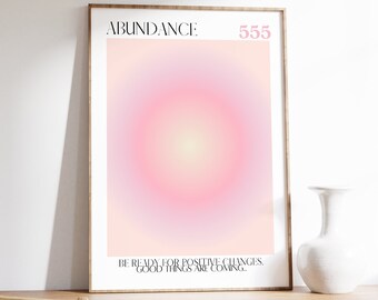 May include: A framed print with a pink and white gradient background and a circle in the center. The text "ABUNDANCE: 555" is at the top of the print. The text "BE READY FOR POSITIVE CHANGES. GOOD THINGS ARE COMING..." is at the bottom of the print.