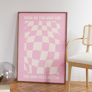 May include: A pink and white checkered poster with the text "Focus on the good and the good gets better" in a retro font.