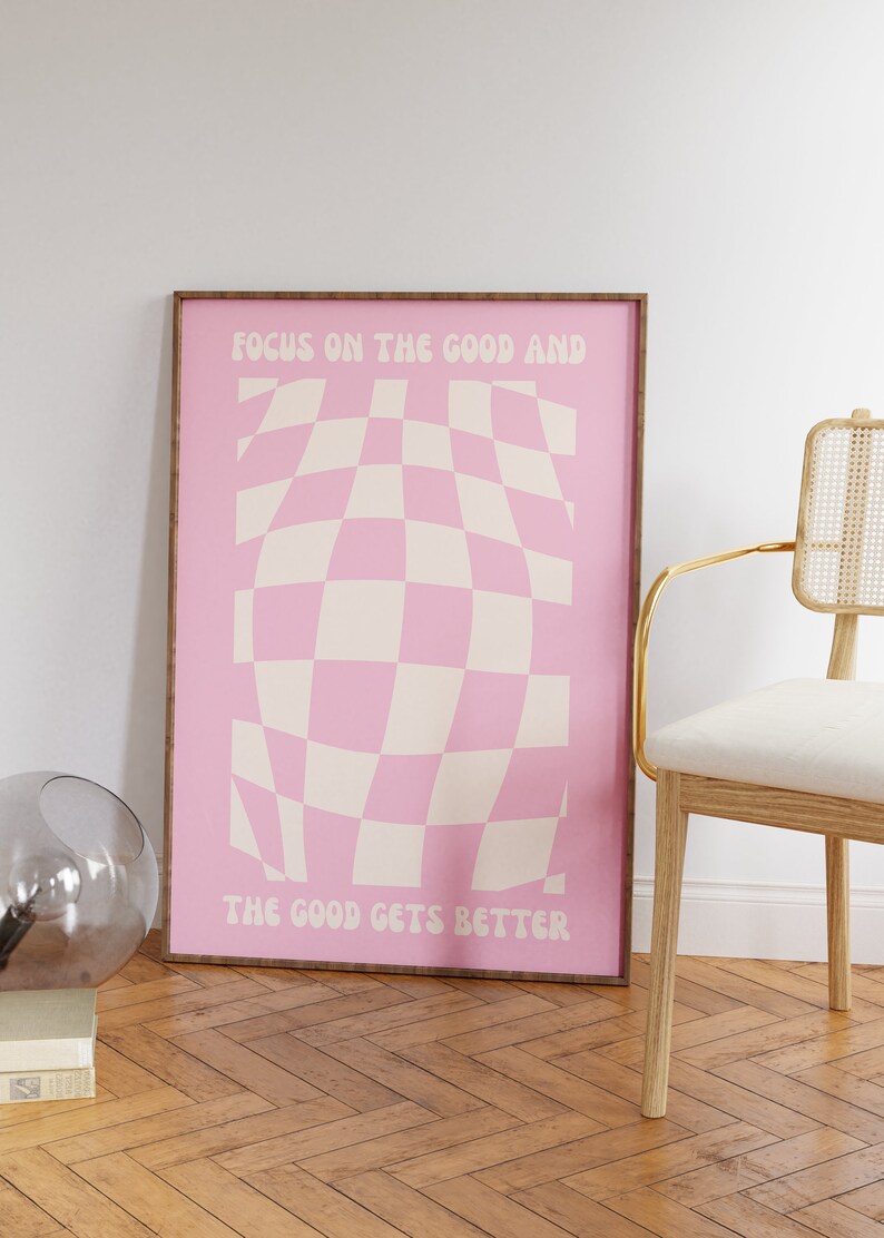 May include: A pink and white checkered poster with the text "Focus on the good and the good gets better" in a retro font.