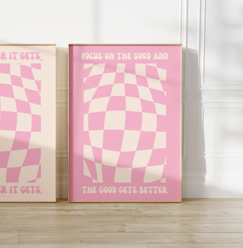 May include: Two pink and cream checkered posters with motivational quotes. The left poster says "_R IT GETS, ER IT GETS." The right poster says "FOCUS ON THE GOOD AND THE GOOD GETS BETTER."