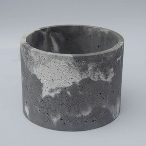 May include: A gray concrete planter with a white marbled design. The planter is cylindrical in shape and has a rough texture.