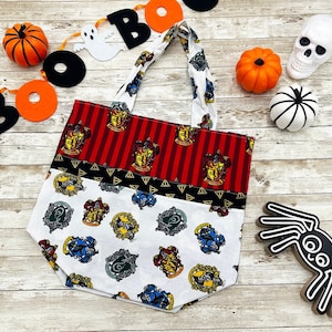 May include: A white and red striped tote bag with a Harry Potter theme. The bag features the Hogwarts house crests and is perfect for carrying everyday essentials.