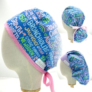 May include: Three blue surgical caps with pink ties. The caps are printed with colorful text, including medical terms like "bronchiolitis", "jaundice", "cystic fibrosis", "newborn", "ADHD", "otitis", "growth charts", "cerebral palsy", and "ASD".