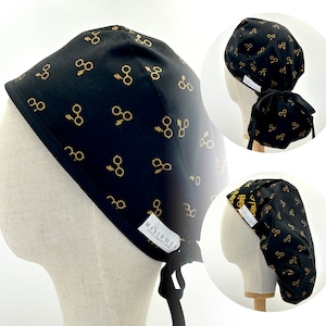May include: Black scrub hat with a gold print of glasses and lightning bolts. The hat has a tie on the back and a label that says "MARIPOSA" and "Handmade in USA".