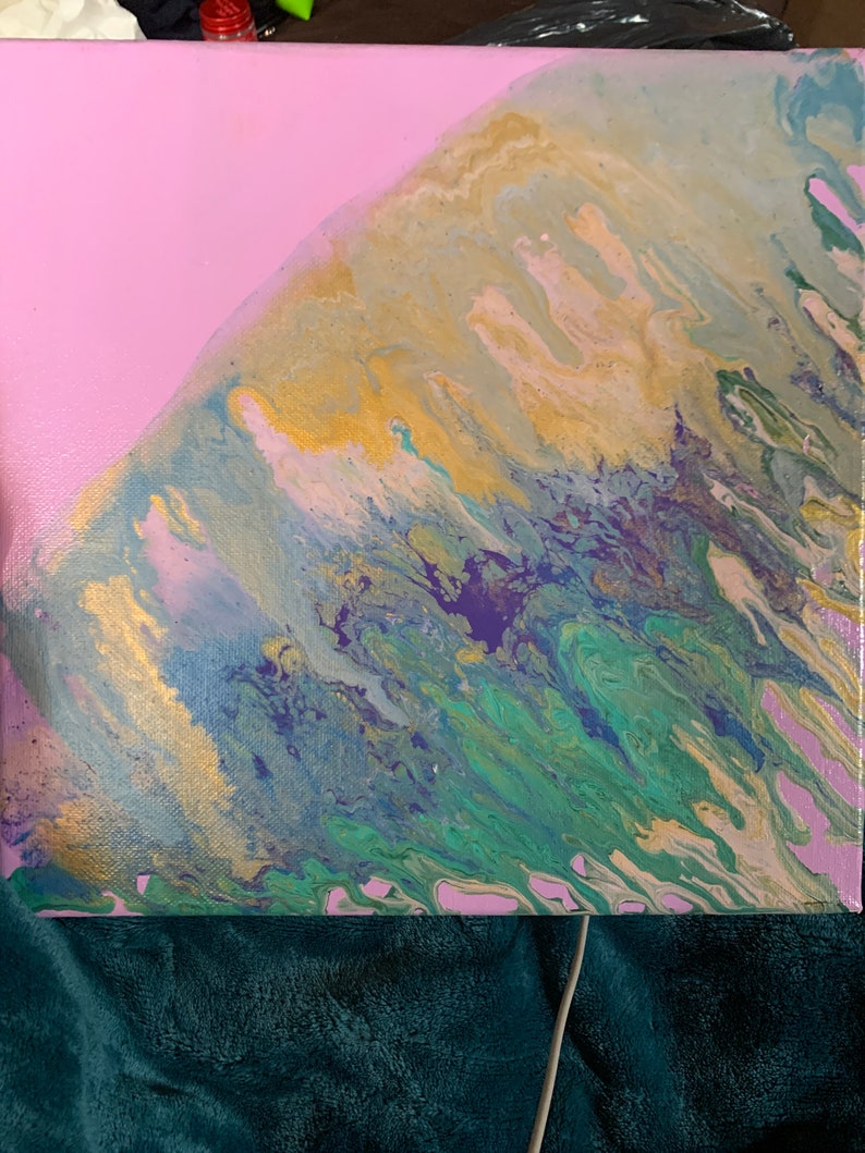 K&ouml;nnte beinhalten: Ein quadratisches Leinwandgem&auml;lde in Acryl-Flie&szlig;technik. Die Komposition zeigt einen einfarbigen hellrosa Bereich, der in eine marmorierte Mischung aus metallischem Gold, T&uuml;rkis, tiefem Violett und Hellblau in wellenartigen Mustern &uuml;bergeht.