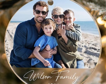 May include: Round, clear glass Christmas ornament with a photo of a family of four on a beach. The ornament has a gold rim and the text "Wilson Family 2024" is printed on the bottom.
