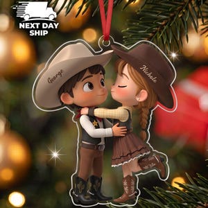 May include: A flat acrylic Christmas ornament featuring a cartoon-style couple dressed in western attire. The figure on the left wears a cream cowboy hat labeled George, while the figure on the right wears a brown cowboy hat labeled Nichole.
