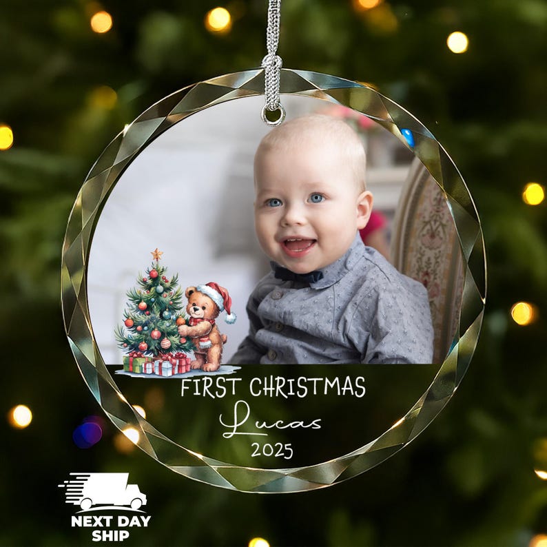 K&ouml;nnte beinhalten: Ein kreisf&ouml;rmiger Weihnachtsbaumschmuck aus Glas mit facettiertem Rand, der ein Foto eines Babys, eine Aquarellillustration eines Teddyb&auml;ren neben einem geschm&uuml;ckten Weihnachtsbaum sowie den Text FIRST CHRISTMAS Lucas 2025 zeigt.
