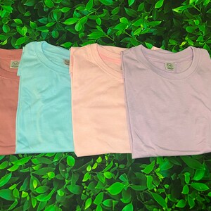 Op de afbeelding: Vier effen T-shirts in verschillende kleuren: poederroze, lichtblauw, roze en lavendel.