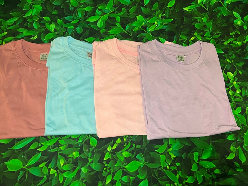 Op de afbeelding: Vier effen T-shirts in verschillende kleuren: poederroze, lichtblauw, roze en lavendel.