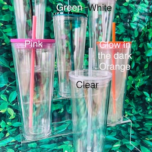 Op de afbeelding: Zes doorzichtige plastic bekers met deksels en rietjes. De deksels zijn in verschillende kleuren: zwart, groen, wit, roze, oranje en transparant. De bekers zijn in een piramidevorm op een doorzichtige acryl displaystandaard geplaatst. De tekst "Nosaleb's Blanks" is op de standaard gedrukt.