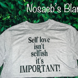 Puede incluir: Una camiseta gris con el texto "Self love isn't selfish it's IMPORTANT!" impreso en negro.