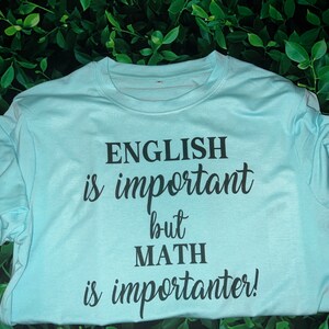 Puede incluir: Una camiseta azul claro con texto negro que dice "El ingl&eacute;s es importante, pero las matem&aacute;ticas son m&aacute;s importantes!"