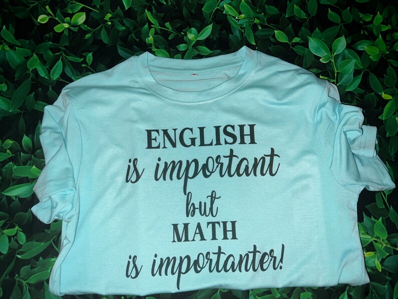 Puede incluir: Una camiseta azul claro con texto negro que dice "El ingl&eacute;s es importante, pero las matem&aacute;ticas son m&aacute;s importantes!"