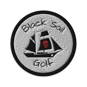 以下が含まれることがあります： 黒と白の刺繍パッチで、海賊船と「Black Sail Golf」の文字が描かれています。