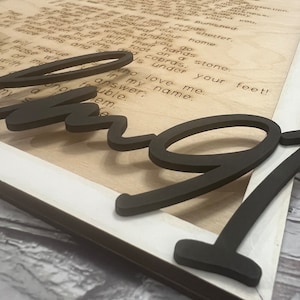 A rectangular white frame with the words from Psalm 91 laser etched onto the wood background. The words "Pslam91" is cut out in script letters and glued over the frame.