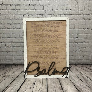 A rectangular white frame with the words from Psalm 91 laser etched onto the wood background. The words "Pslam91" is cut out in script letters and glued over the frame.