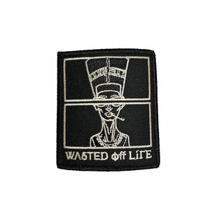 May include: Black and white embroidered patch with a stylized image of a person wearing a crown and smoking a cigarette. The text "WASTED off LIFE" is below the image.
