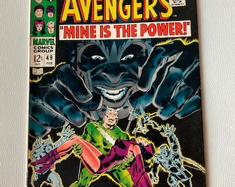 Puede incluir: Una portada de cómic con los Vengadores, un grupo de superhéroes. La portada es negra y presenta una figura grande y amenazante con una cara oscura y sombría. El texto de la portada dice "The Avengers" y "Mine is the Power!"