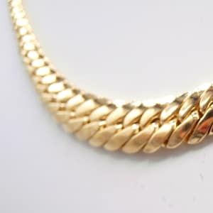 May include: A gold chain necklace with a thick, flat, curb link design.