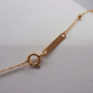 May include: Close-up of a delicate gold necklace with a small chain and a round clasp. The necklace features a small rectangular tag with the word "UNOAErre" engraved on it. The necklace is on a white background.