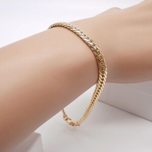 Pode incluir: Um bracelete de corrente de ouro com um design trançado.