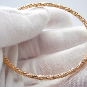 May include: A gold bangle bracelet with a twisted, textured design. The bracelet is open and has a hinged clasp.