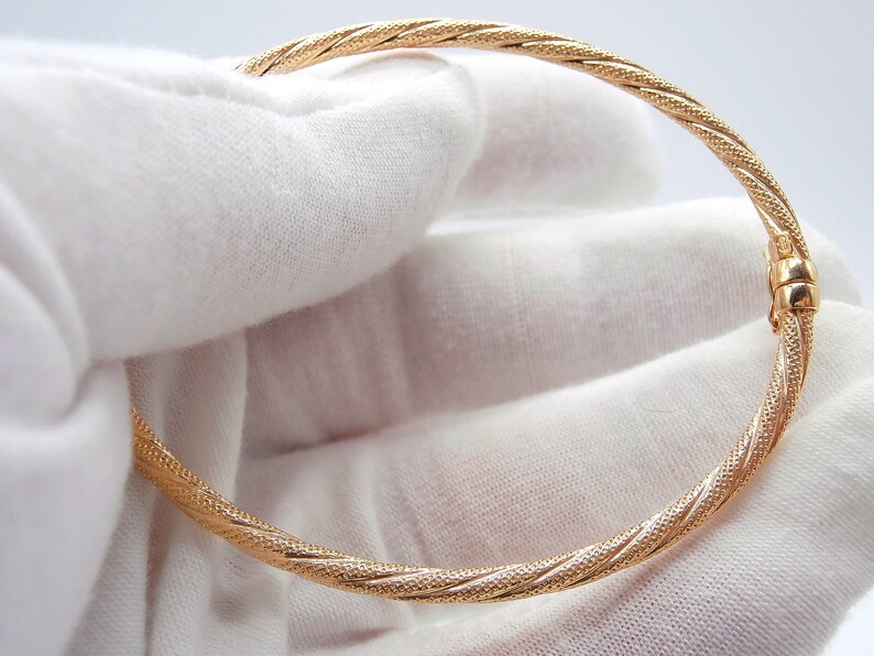 May include: A gold bangle bracelet with a twisted, textured design. The bracelet is open and has a hinged clasp.