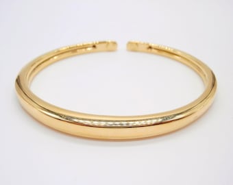 Puede incluir: Un brazalete de oro simple con una superficie lisa y redondeada.