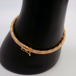 May include: A gold bangle bracelet with a twisted design. The bracelet has a clasp closure.