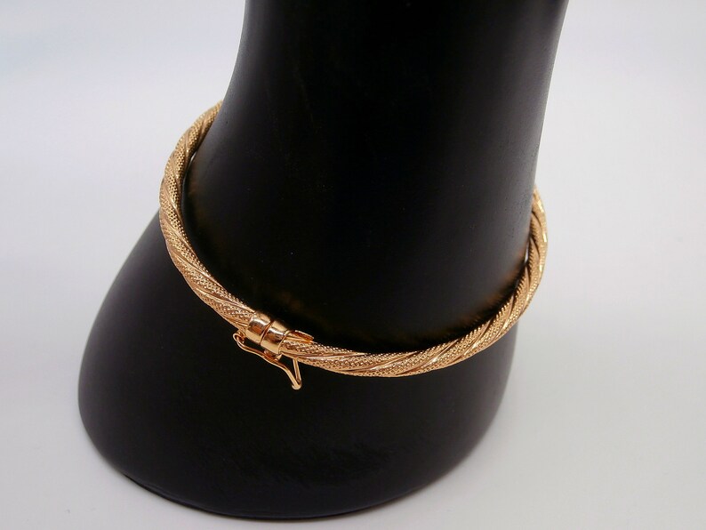 May include: A gold bangle bracelet with a twisted design. The bracelet has a clasp closure.