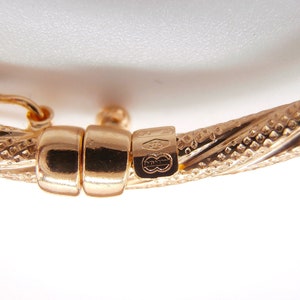May include: Close-up of a gold bangle bracelet with a twisted design and a clasp. The bracelet is marked with "375" and a logo.