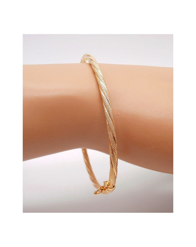 May include: A gold bangle bracelet with a twisted design. The bracelet is made of a smooth, shiny metal and has a simple, elegant look.