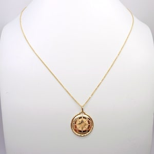Può includere: Una collana con catena d'oro con un ciondolo rotondo che presenta un design a rosa dei venti. Il ciondolo è inciso con le parole "Nord, Sud, Est, Ovest".