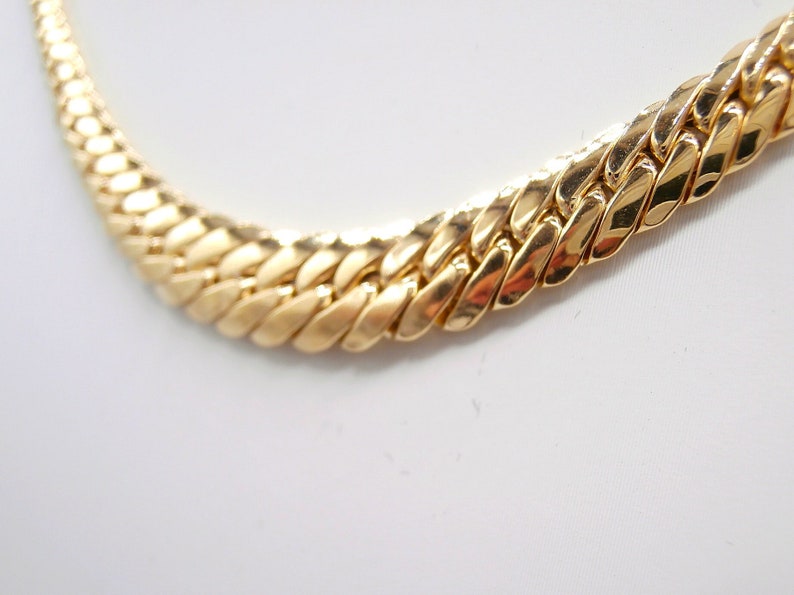 May include: A gold chain necklace with a thick, flat, curb link design.