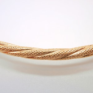 May include: A gold bangle bracelet with a twisted design and a textured surface.