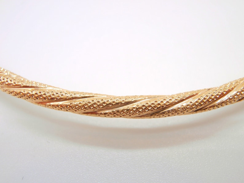 May include: A gold bangle bracelet with a twisted design and a textured surface.