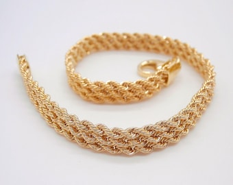 May include: A gold-colored rope chain necklace with a clasp. The necklace is made of tightly woven strands, creating a textured appearance. The chain is displayed on a white background.