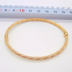 May include: A gold bangle bracelet with a twisted design. The bracelet is approximately 10 inches in diameter.
