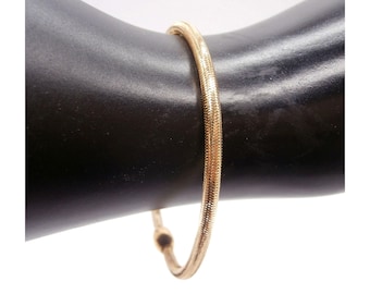 May include: A gold-colored, textured bracelet. The bracelet is a continuous loop, with a snake-chain design. The bracelet is displayed on a black surface.