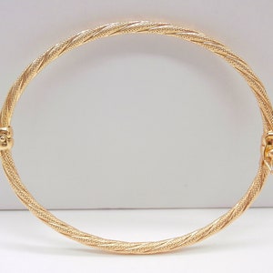 May include: A gold bangle bracelet with a twisted design. The bracelet has a hinged clasp.