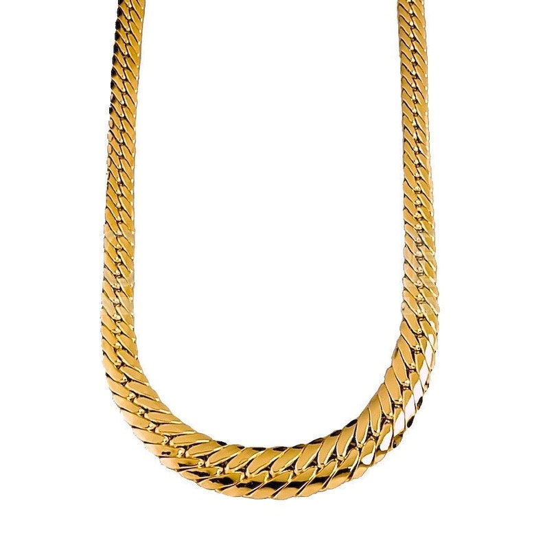 May include: A gold chain necklace with a thick, flat, and textured design. The chain is made of interlocking links that create a bold and eye-catching look.