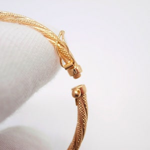 May include: A gold bangle bracelet with a twisted design and a clasp closure.