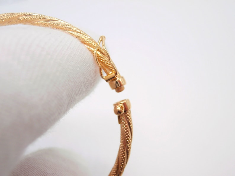 May include: A gold bangle bracelet with a twisted design and a clasp closure.